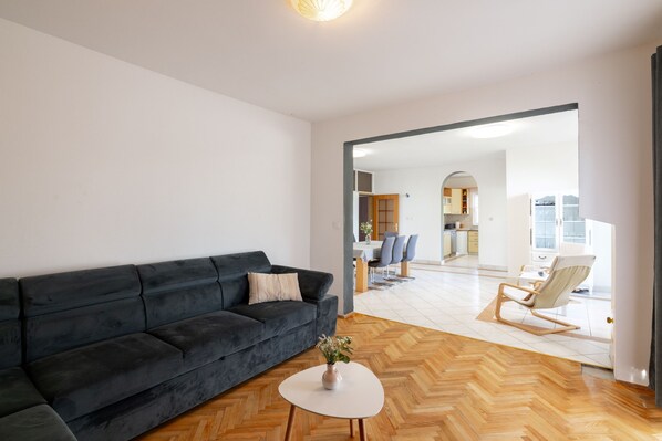 A modern living room with a dark sofa, a white coffee table, and a view into the dining area.