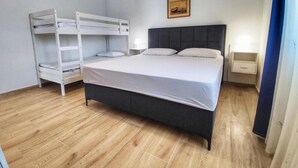 A bedroom with a bunk bed, a single bed, a bedside table with a lamp, and a framed picture on the wall.