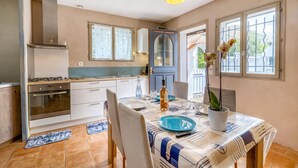 A modern kitchen with a gas stove, oven, and white cabinets. There is a dining table set with plates, glasses, and a bottle.