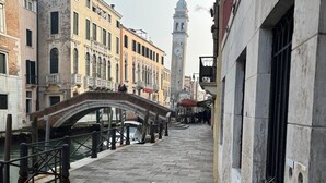 Un étroit canal vénitien, avec un pont de pierre, des bâtiments historiques et, au loin, un beffroi.