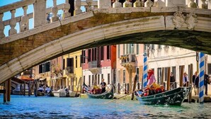 Un pont historique enjambant un canal où naviguent des gondoles et des bateaux, le tout entouré d’immeubles aux couleurs vives.