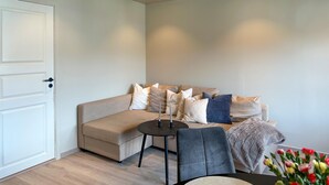 Ein modernes Wohnzimmer mit einem beigefarbenen Ecksofa, einem runden schwarzen Couchtisch und einem grauen Sessel.