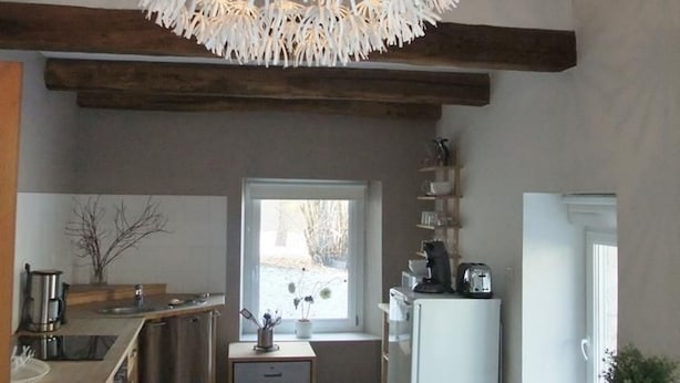 A kitchen with a modern chandelier, wooden beams, a window with a view, and a refrigerator with kitchen appliances.