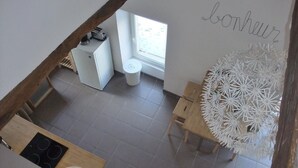 A kitchen with a stove, sink, and a window. There is a decorative white piece on the wall and a wooden table with a chair.