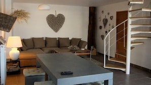 A modern living room with a sofa, a coffee table, a lamp, a heart-shaped wall decoration, and a spiral staircase.