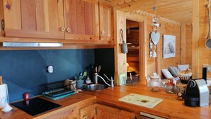 A wooden kitchen with a built-in oven, a sink, and a dishwasher. There are wooden cabinets, a countertop with various kitchen items, and a hanging light fixture. - 3-room apartment for 7 people, renovated, sunny balcony (Pra-Loup)
