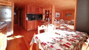 A cozy cabin interior with wooden walls and ceilings, a kitchen area, a dining table with chairs, and a sofa in the living area. - 3-room apartment for 7 people, renovated, sunny balcony (Pra-Loup)