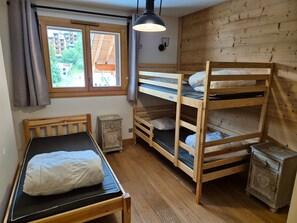 Habitación tipo dormitorio con literas, una cama individual, una mesita de noche pequeña, una lámpara y una ventana con cortinas.
