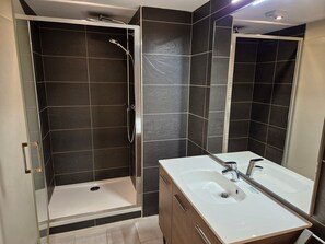 Un baño moderno con cabina de ducha de vidrio, lavamanos blanco y paredes cubiertas de baldosas oscuras.