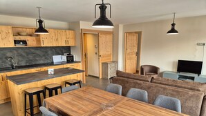 A modern kitchen with wooden cabinets, a central island, and bar stools. There is a dining area with a wooden table and grey chairs. - Bright apartment near slopes, pets allowed (Les Deux Alpes)