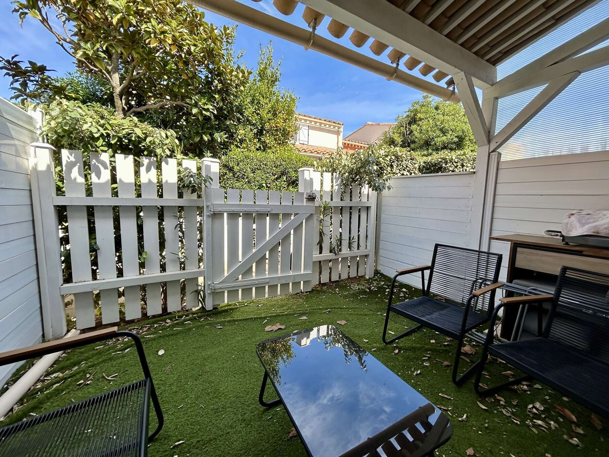 A covered patio with a white fence, a table, and two chairs.