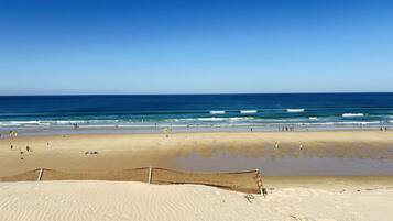 Een strand met een zandgebied en een afgesloten gedeelte, vermoedelijk voor beachvolleybal of vergelijkbare activiteiten.