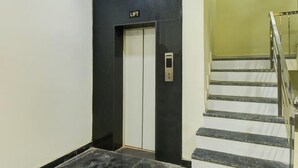 Een lift met een 'LIFT'-bord, een wenteltrap met een metalen leuning, en een muur met een zwart paneel.