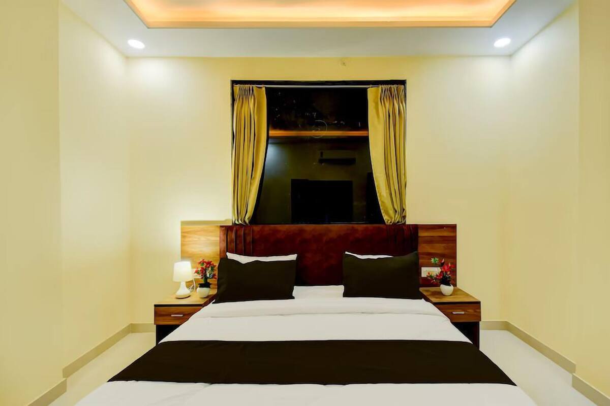 A hotel room with a large bed, wooden headboard, two bedside tables with lamps, and a window with curtains.