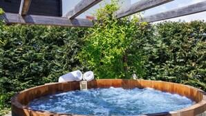 Ein hölzernes Whirlpool mit integriertem Heizsystem, umgeben von üppiger Vegetation und einer überstehenden Holzpergola.