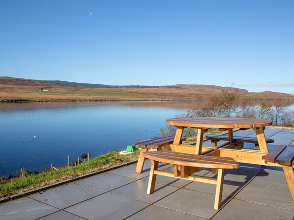 Une table de pique-nique en bois avec des bancs, située au bord d’un lac.