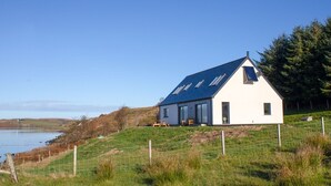 Une maison moderne avec un toit en pente, de grandes fenêtres et une vue sur la mer.