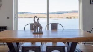 Une table à manger avec des chaises, donnant sur un lac grâce à une grande fenêtre.