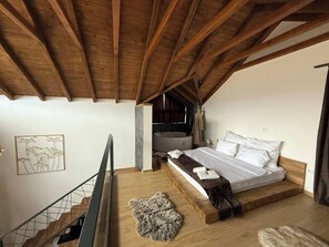 Une chambre avec un plafond en bois, un lit recouvert de draps blancs, un mur en pierre et une baignoire.