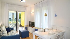 Ein modernes Wohnzimmer mit einer Couch, einem Esstisch für zwei Personen und einem Fernseher.