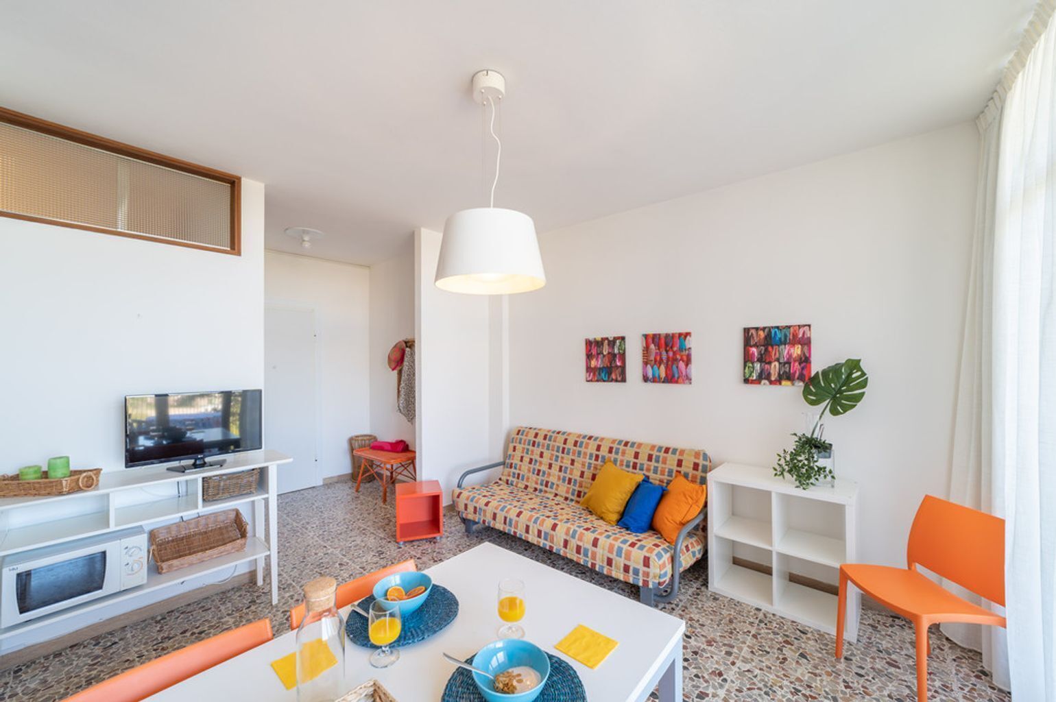 A modern living room with a television, sofa, dining table, and various decorative items.