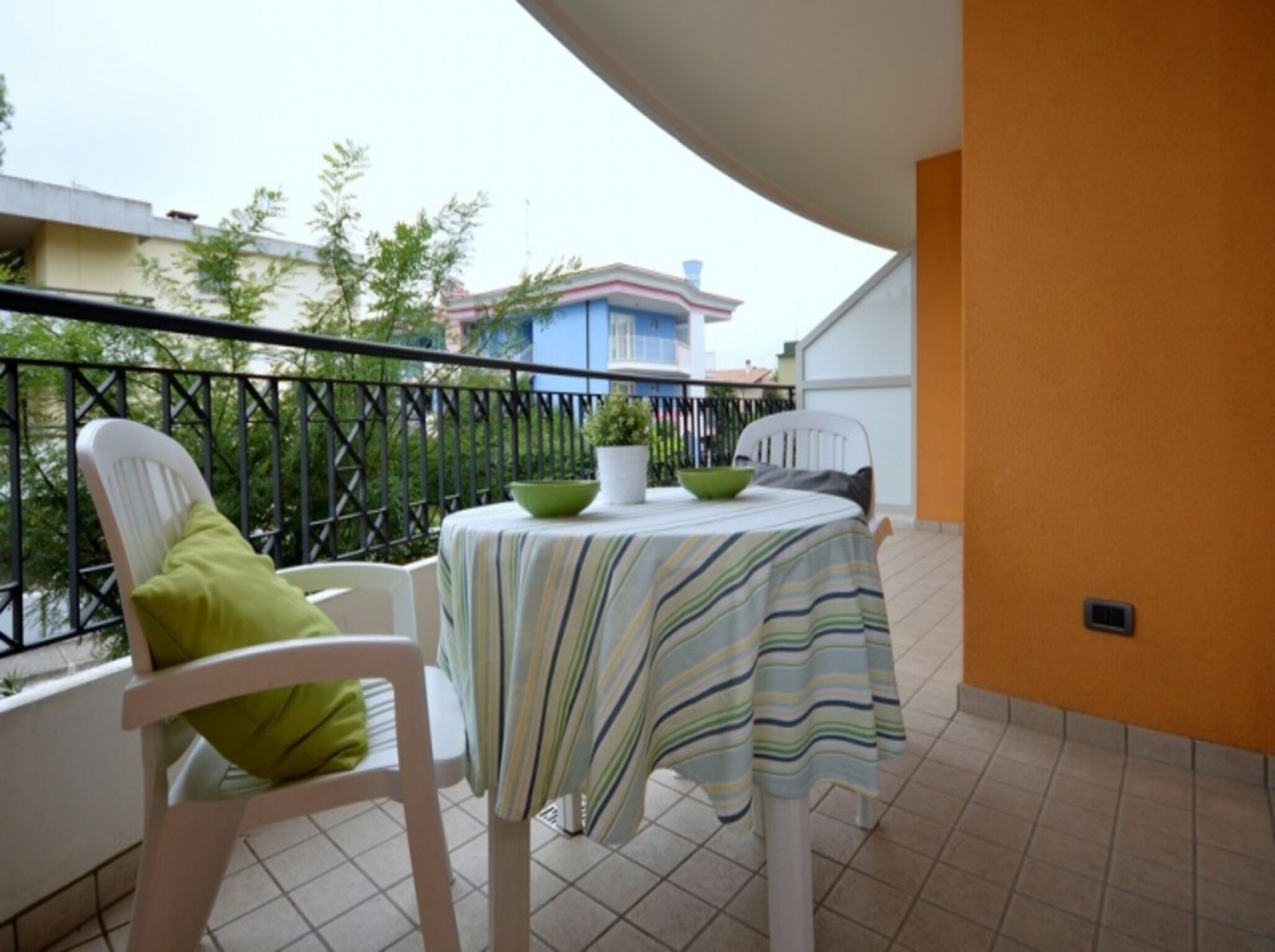 Ein Balkon mit Tisch und Stühlen, einem Blumentopf und Blick auf Gebäude im Hintergrund.