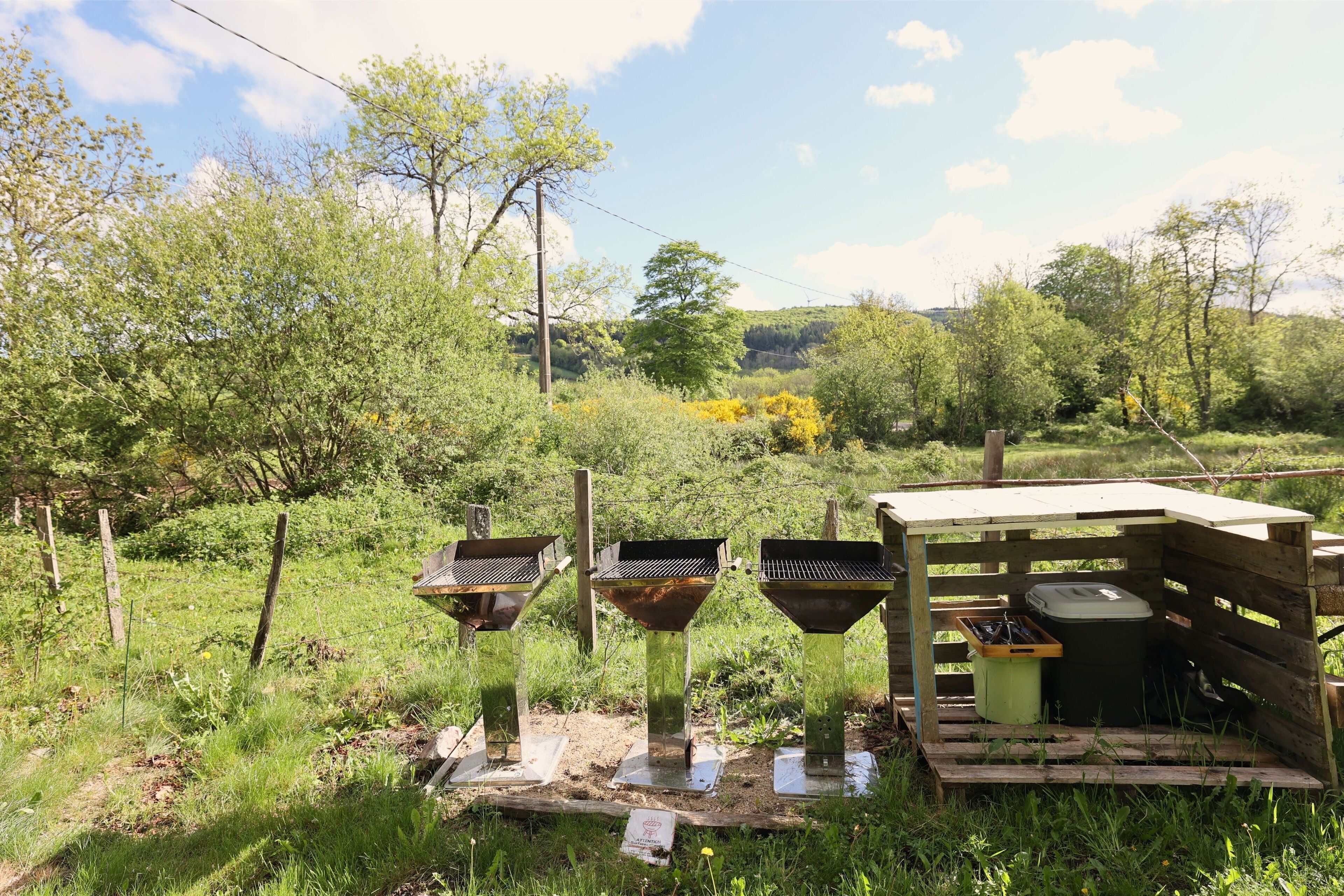 A rustic outdoor setting with three metal funnels and a wooden structure, surrounded by greenery and trees.