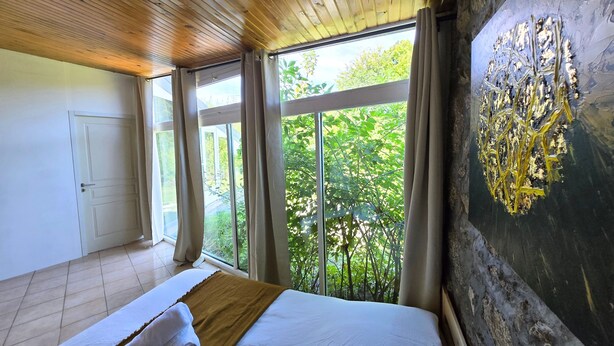 Een slaapkamer met een groot bed, uitzicht op groen en een houten plafond.