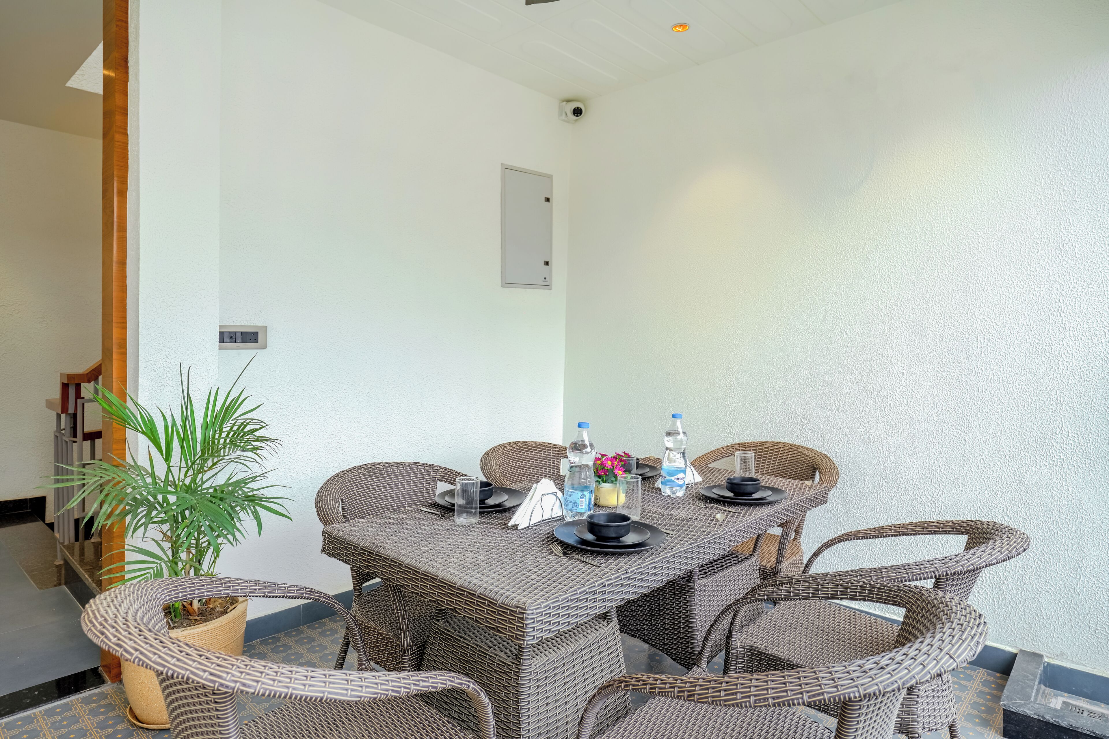 A dining area with a wicker table and chairs, a potted plant, and a water bottle on the table.