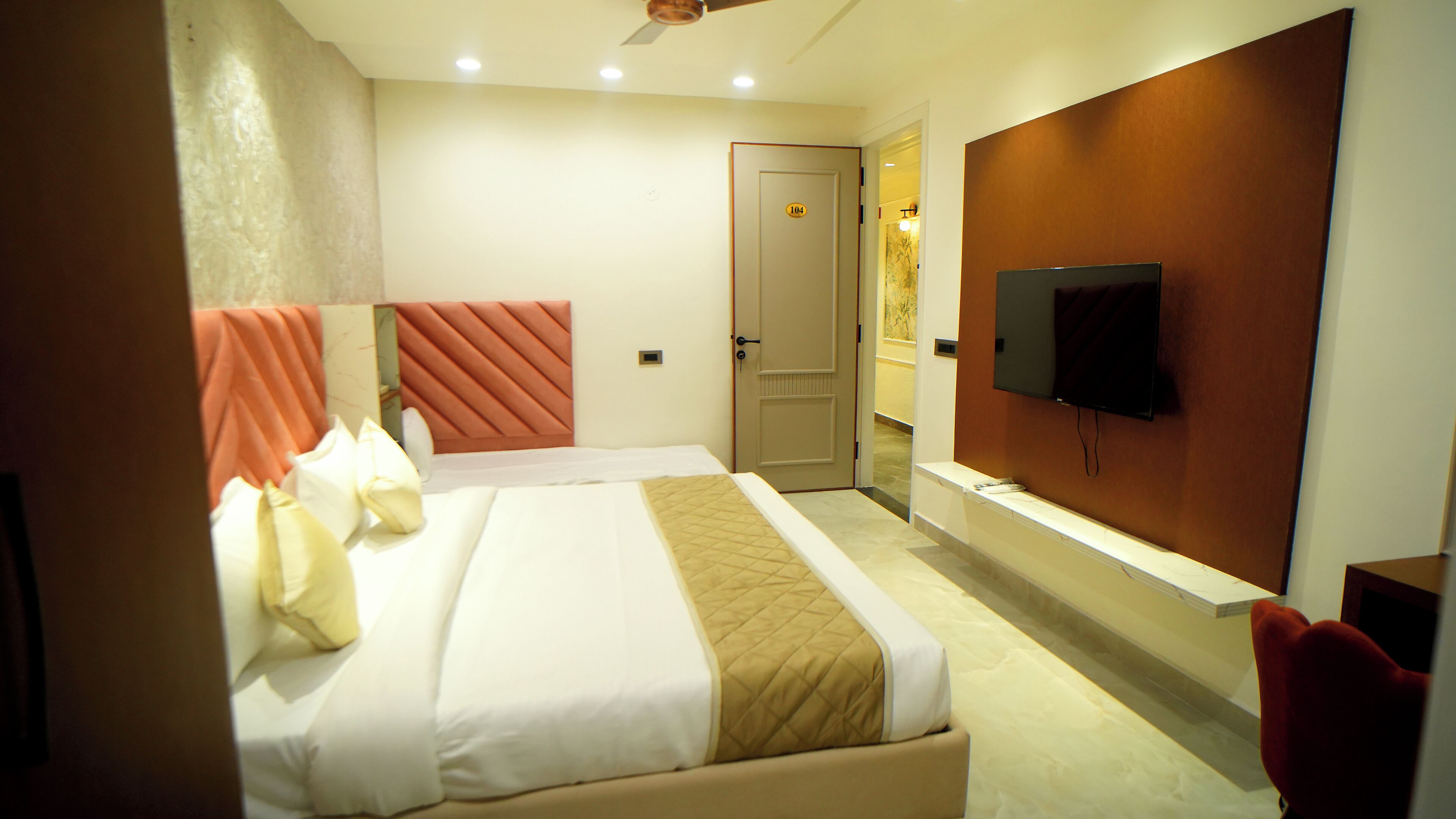 A hotel room with a bed, a TV, a door, and a mirror.