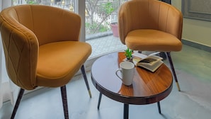 A room with two leather chairs, a small wooden table, a potted plant, and a window with curtains. - HOTEL ELEGANCE (Amritsar)