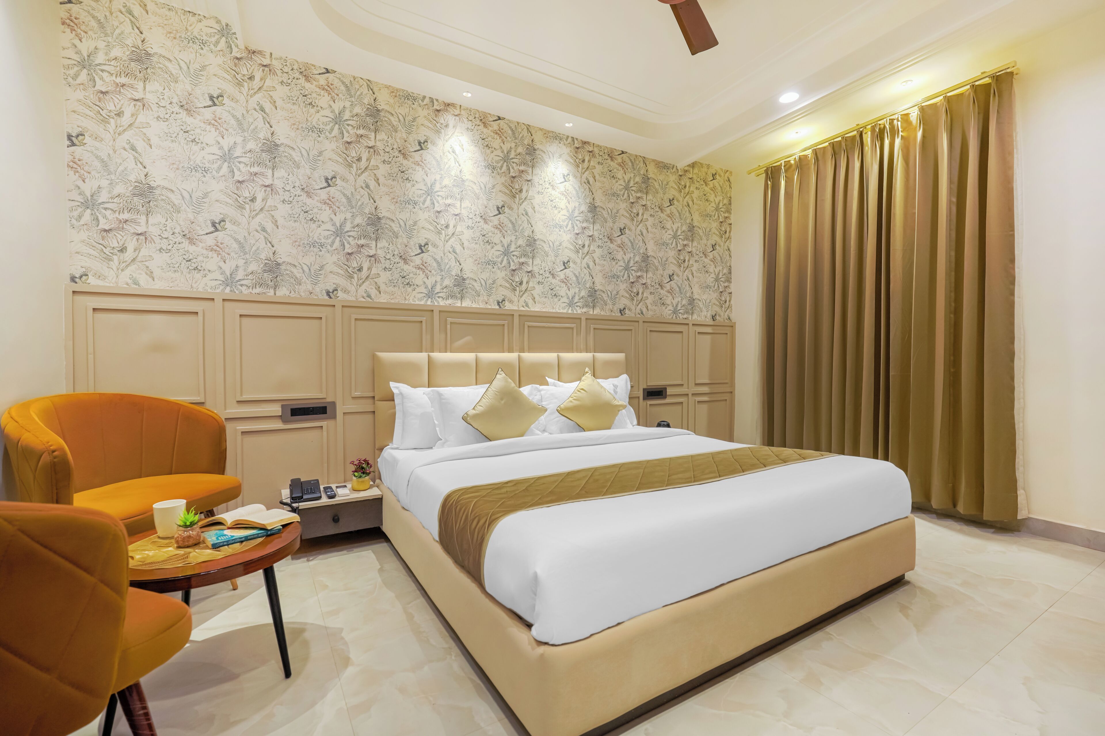 A hotel room with a bed, a nightstand, a chair, and a small table with a plant and a book.