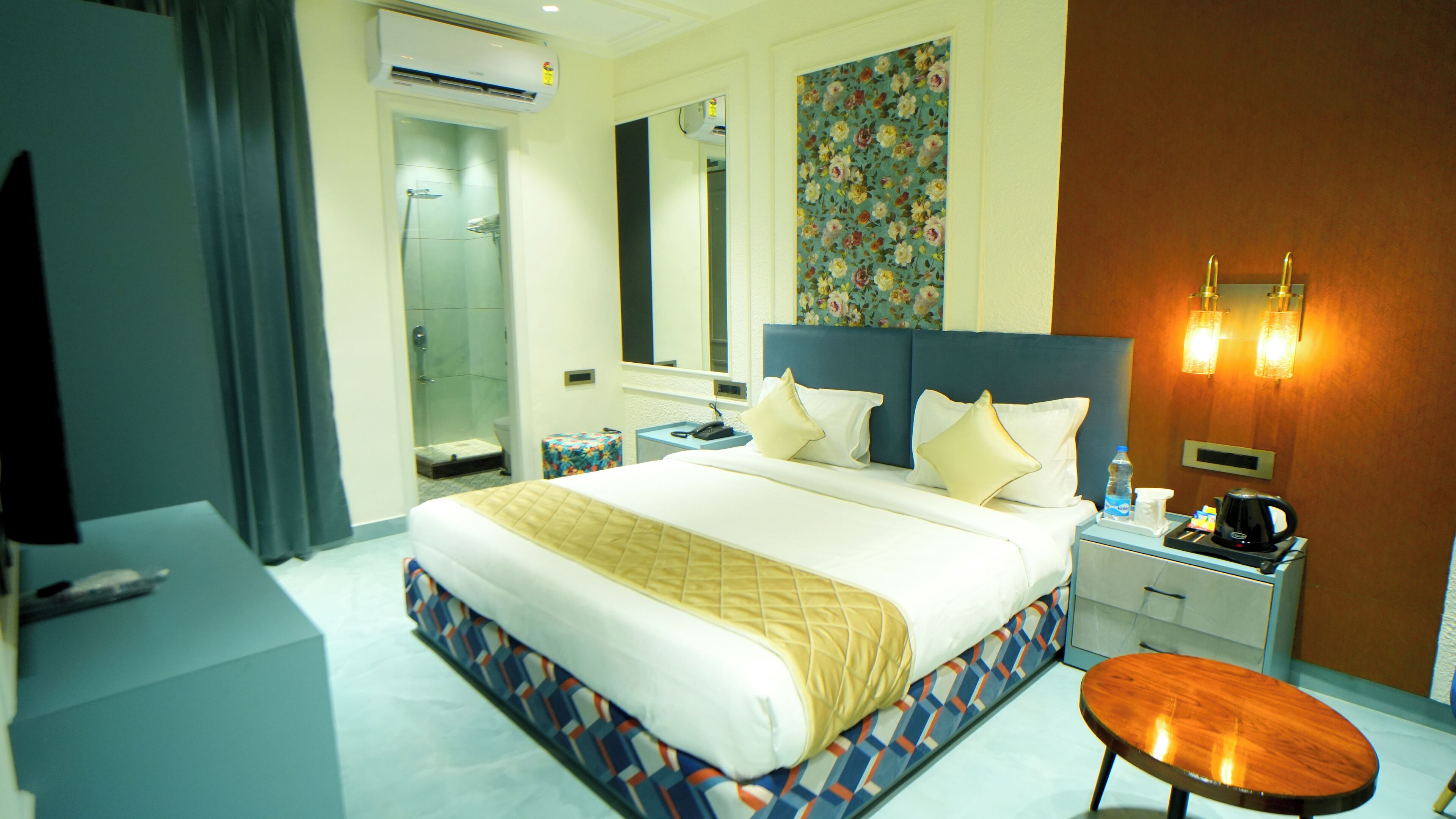 Une chambre d’hôtel avec un grand lit, une table de chevet avec une machine à café, une commode, un miroir et un espace douche.