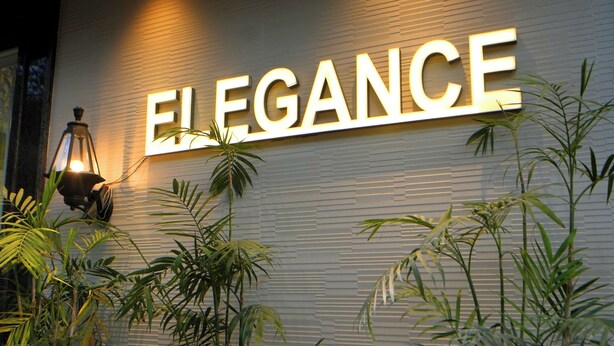 A wall with the word "ELEGANCE" illuminated in large letters, flanked by potted plants. - HOTEL ELEGANCE (Amritsar)