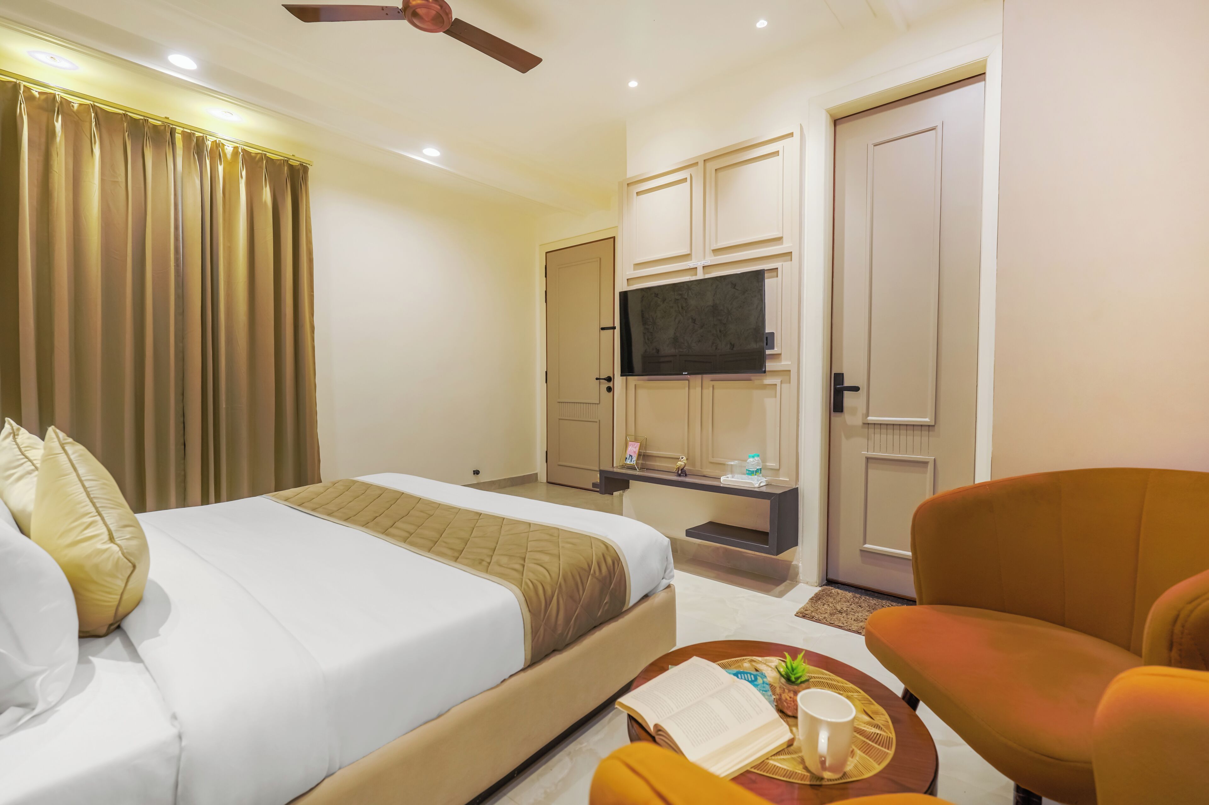 Quarto de hotel com cama, escrivaninha, televisão, cadeira e ventoinha no teto.