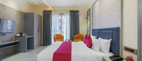 Una habitación de hotel con cama, escritorio, silla, televisión, ventilador de techo y ventana con cortinas.