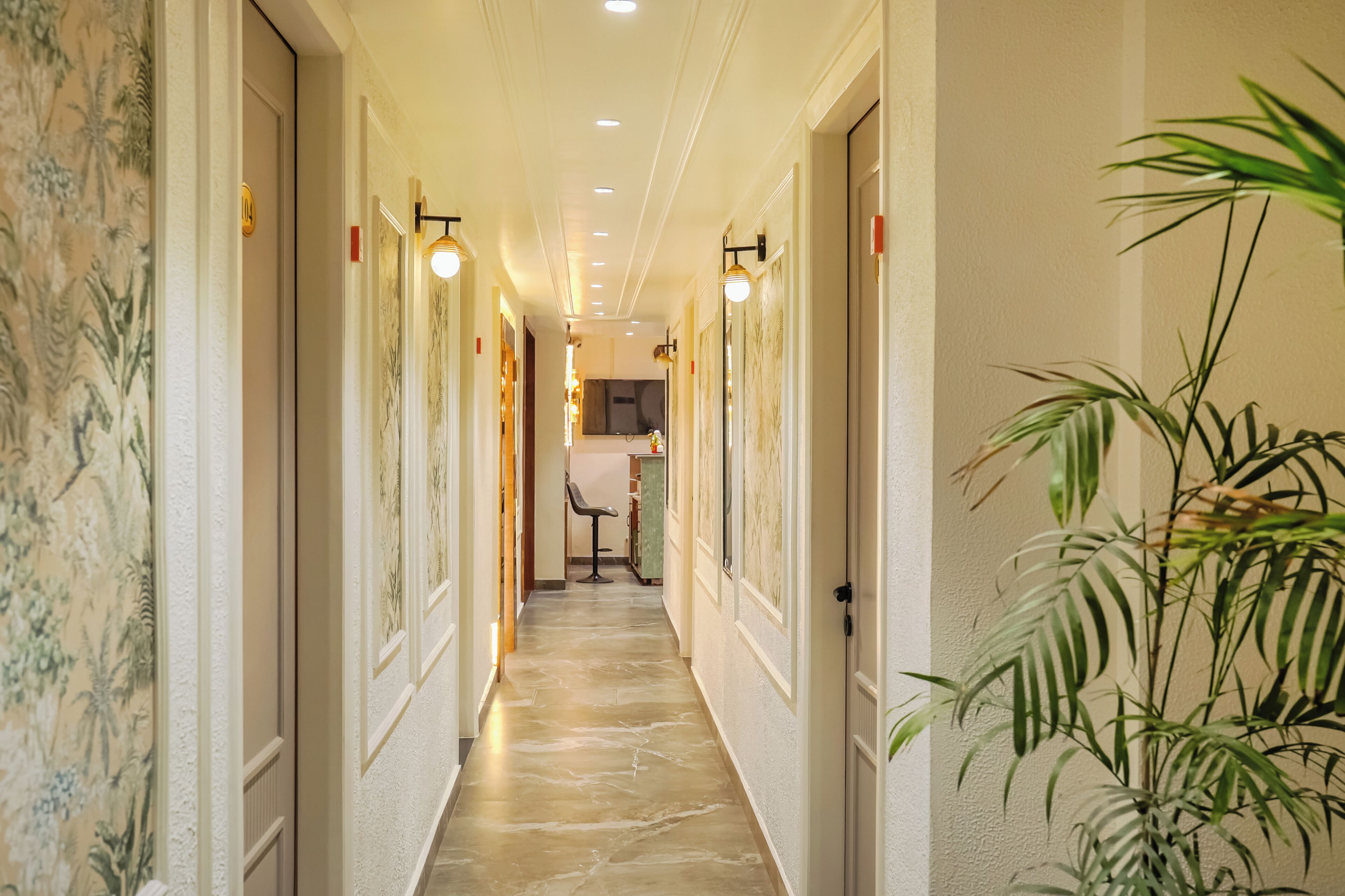 A hotel hallway with a marble floor, wall-mounted light fixtures, and a potted plant.