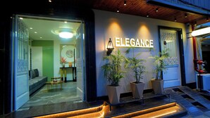 A hotel entrance with a sign reading "Elegance," a reception desk, and potted plants. - HOTEL ELEGANCE (Amritsar)