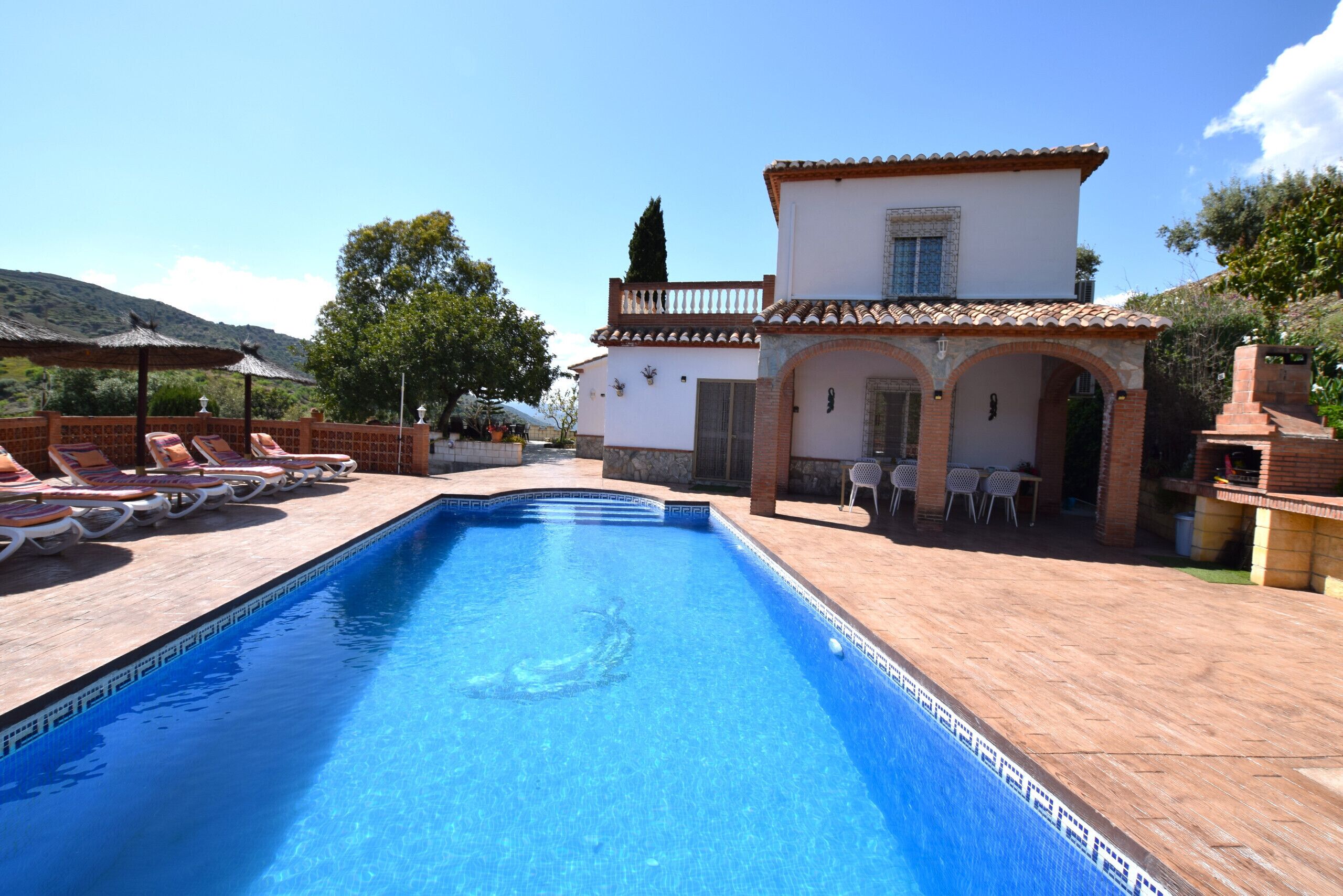 A swimming pool with lounge chairs, a patio area, and a building with arched doorways.