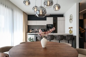 Una cucina moderna con zona pranzo, caratterizzata da un tavolo rotondo in legno, un vaso con fiori e illuminazione a sospensione.