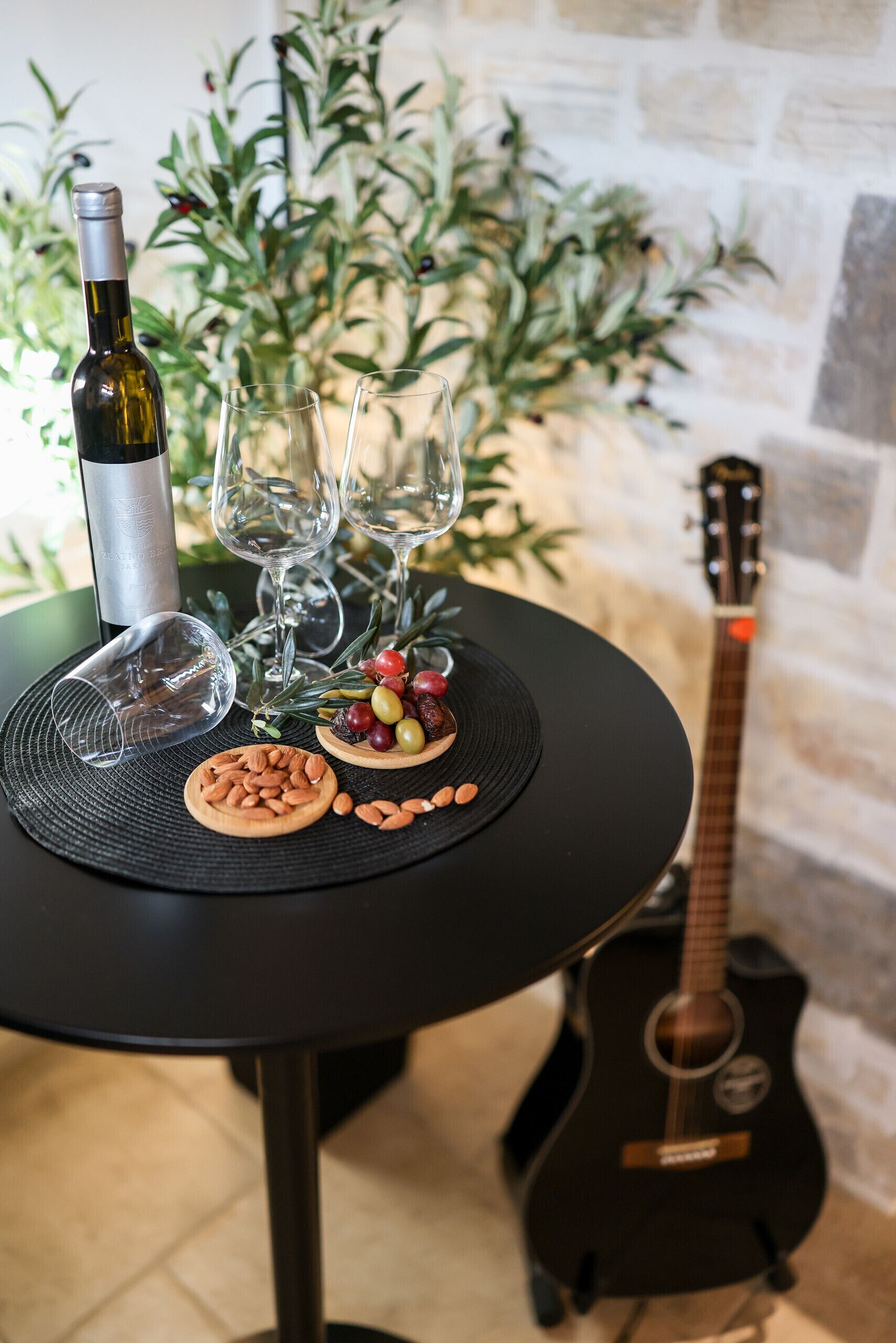 Une table avec une bouteille de vin, des verres, des amandes et des olives. Une guitare est visible à l’arrière-plan.