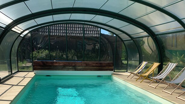 Una piscina amb sostre de vidre, envoltada de gandules i un pont de fusta.