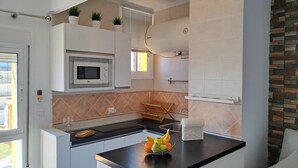 A modern kitchen with a microwave, a fruit bowl, and a window with blinds. - Beachfront studio (Calahonda)