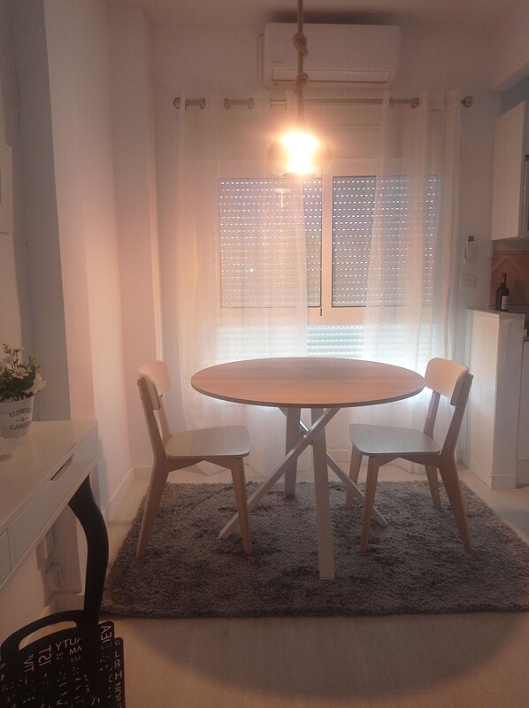 A dining area with a round table and four chairs, a white cabinet, and a window with blinds. - Beachfront studio (Calahonda)