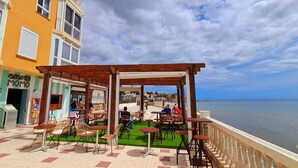 An outdoor cafe with tables and chairs, overlooking a body of water. - Beachfront studio (Calahonda)