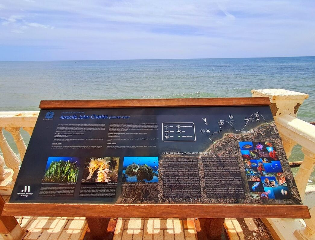 An informational sign about Arrecife John Charles, featuring text and images of marine life and underwater scenes.