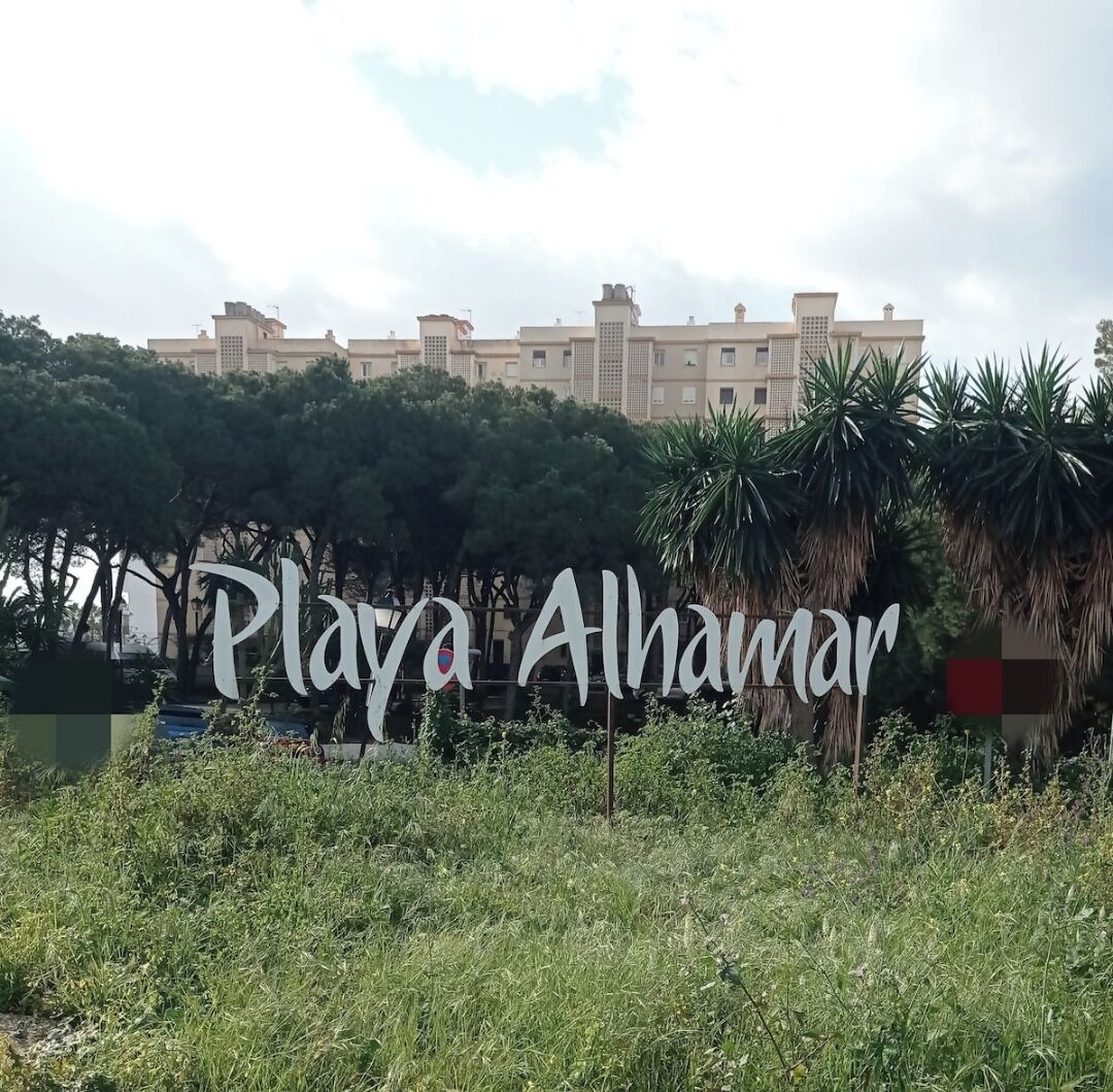 Letrero de Playa Alhamar con edificios residenciales y palmeras al fondo.
