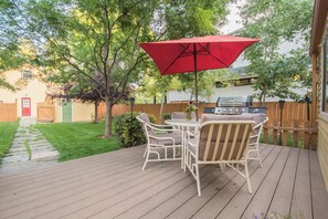 Un patio in legno con tavolo e sedie, un ombrellone rosso e un barbecue.
