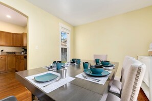 Comedor con una mesa lista para cuatro personas, armarios de madera y una ventana con persianas.