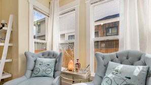 A room with two grey upholstered chairs, each with a bicycle-themed pillow. A small table with a candle and glasses is placed between the chairs. - Spacious Old Town Home Walk to Dining & Culture! (Fort Collins)